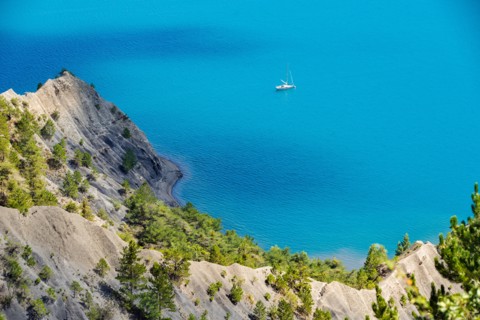 Serre-Poncon Lake in summer with deep blue water and sailing boat. Hautes-Alpes, PACA Region, Southern French Alps, France