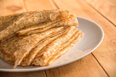 Close up on a stack of folded crepes (french pancakes) on a plate, wooden background