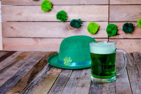 Mug of green beer with Irish festive hat on wooden background. Tabletop, front view.