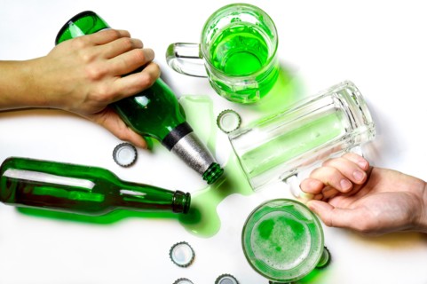 St. Patrick Day after party concept. Glasses and bottles of green beer on messy white table with beer caps