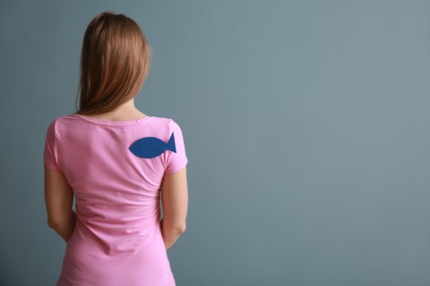 Woman with paper fish on her back against color background. April fools' day prank