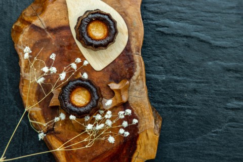 Cannelés (Canelés) de Bordeaux Recipe is a small pastry with rum and vanilla on a wooden plate. Traditional French sweet dessert. tasty snacks. Top vi