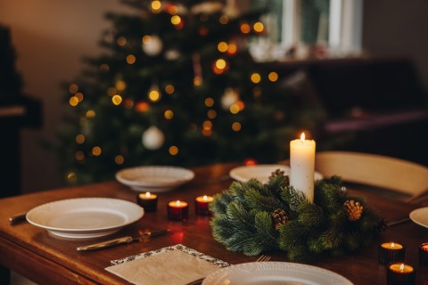 Christmas candles in advent wreath with plates on dinner table. Scandinavian home decorated for Christmas dinner.