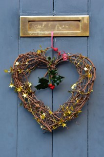 Christmas heart-shaped decoration hangs from festive red ribbon on a wooden door in the picturesque town of Ludlow, Shropshire, England, UK.
