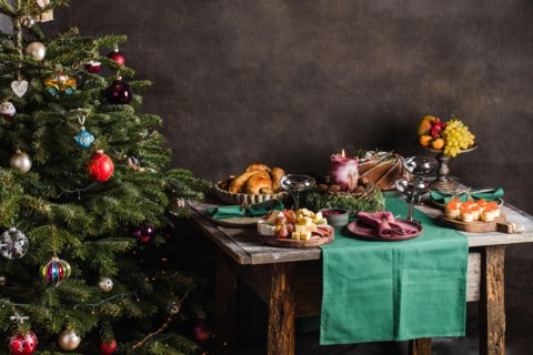 Stylish table setting for christmas family dinner with christmas tree on the background and gifts on the chair.