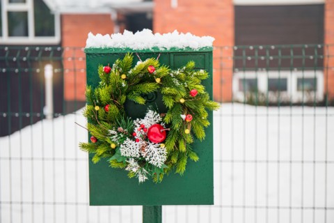 Domestic mail box decorated with spruce tree Christmas wreath outdoors in snowy winter day. Holiday moods.