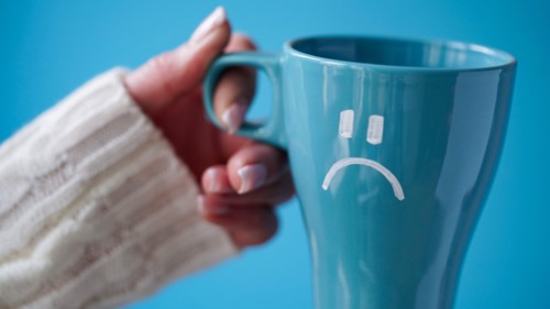 Blue Monday concept. Close-up of a female hand in a white sweater holds a blue cup with a sad smiley as a symbol of the most depressive day of the yea