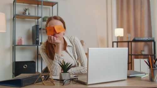 Tired woman teacher using laptop computer with funny stickers on eyes sleeps at workplace, napping