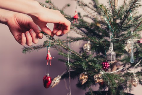 Hands decorating a christmas tree with all kinds of colorful things