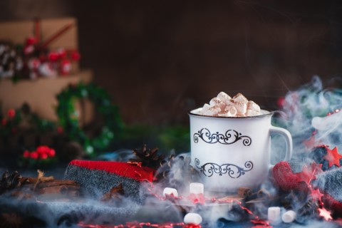Hot chocolate with marshmallows in a cozy enamel mug with steam and Christmas decorations