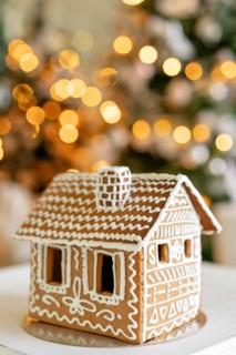 Gingerbread house on table. Defocused lights of Christmas tree. Morning in the bright living room. Holiday mood.