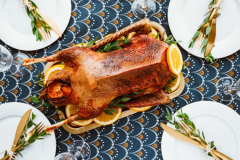 Festive table setting with whole roasted goose on a golden tray for celebrate event or Christmas family dinner. Top view, flat lay.