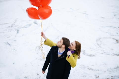 caucasian couple take a walk at winter street, celebrating saint valentines day outdoors. happy man and woman with red air balloons, on a romantic dat