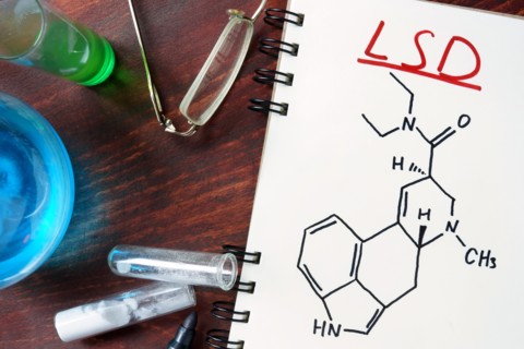 Notepad with chemical formula of LSD on the wooden table. Drugs concept.