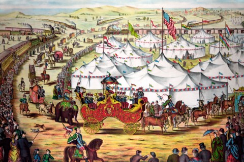 The grand lay-out - Circus parade around tents, with crowd watching alongside railroad train.