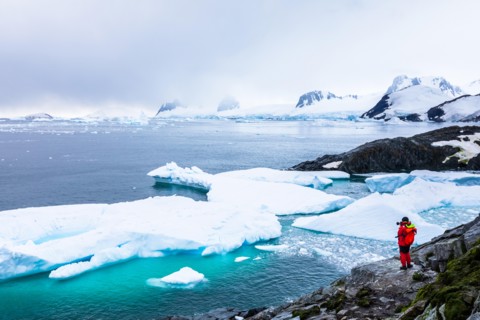 Tourist taking photos of amazing frozen landscape in Antarctica with icebergs, snow, mountains and glaciers, beautiful nature in Antarctic Peninsula w