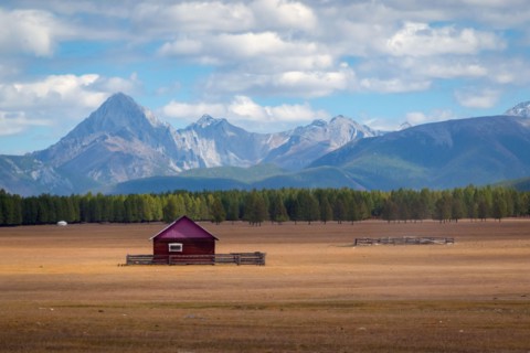 House in the countryside with the mountains in the background. Farm cabin in the rural country surrounded by forest and hills with the snowy tops.