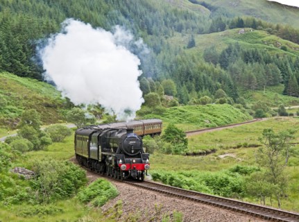 Jacobite steam train moves up hill beyond Glenfinnan Station towards Mallaig on a sunny summer day