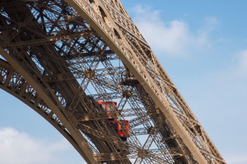 Two bright red elevators climbing up one of Eiffel Tower iron girders bringing tourists to the first floor