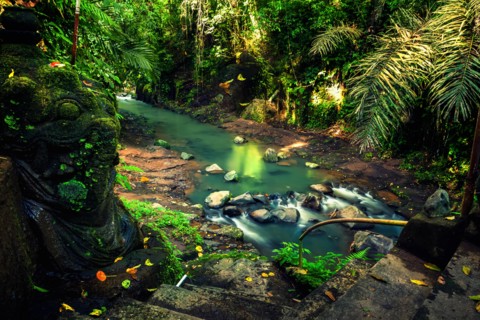 Secret waterfall hidden in tropical jungle with traditional old stone statue on background scenery nature