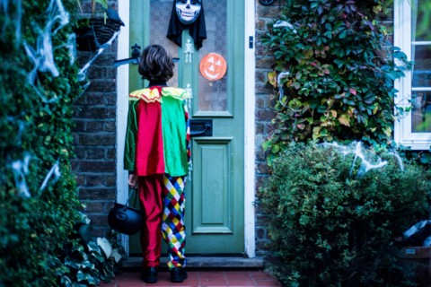 Young boy in halloween costume, standing at door, trick or treating, rear view