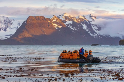 sunset on the snow capped mountains of the bay of isles in south Georgia in the foreground is a zodiac boat from an Antarctic cruise ship
