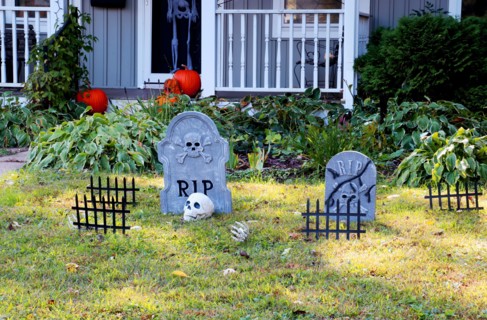 Front yard of private house decorated by fake skull, bones hands, tombstones and grates, pumpkins on the porch for a old american trick-or-treat Hallo