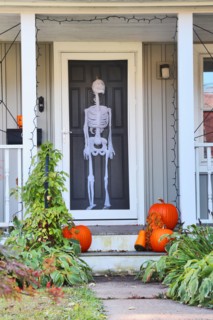 Private house front door with fake skeleton and stair with bright pumpkins decorated for an old american trick-or-treat Halloween tradition. Vertical