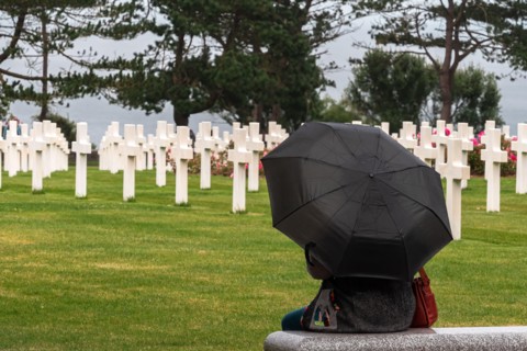 Colleville sur Mer, France - August 5, 2021: Woman with black umbrella meditating at the american Cemetery lined with crosses at Corlleville Sur Mer,
