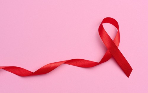 A silk red ribbon in the form of a bow on a pink background, a symbol of the fight against AIDS and a sign of solidarity and sup