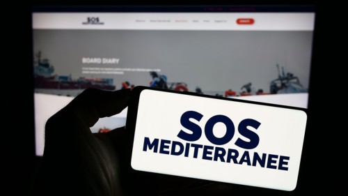 Person holding cellphone with logo of French sea rescue organisation SOS Mediterranee in front of webpage. Focus on phone display.