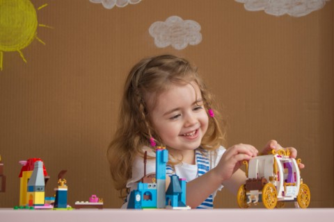 Cute funny preschooler little girl playing with construction toy blocks in kindergarten room. background painted by the sun and clouds