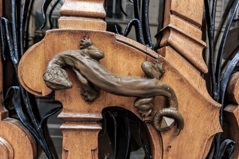 Ornate art nouveau wooden door detail with organic motif and a bronze figurine of a lizard for a door handle in Paris, France