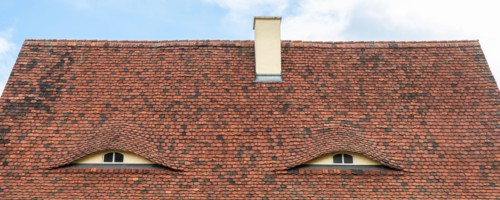 Old beautiful european german fachwerk building rooftop with eye shaped windows and chimney. Typical traditional ancoent house roof architecture in