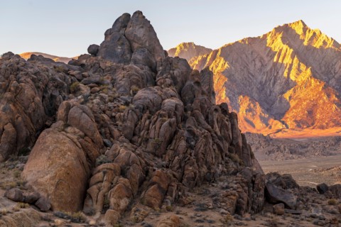 Ancient rock formations of Alabama Hills in foreground with desert expanse and Sierra Nevada mountains in background with alpenglow