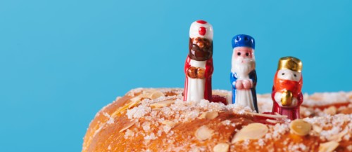 the three wise men, melchior, caspar and balthazar, on top of a roscon de reyes, the spanish king cake, on a blue background in a panoramic format to