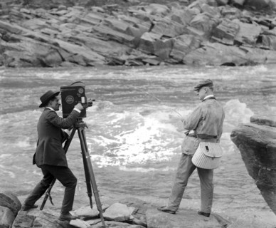 Archival Photo: A man with a film camera filming Senator Miles Poindexter fishing ca. 1918-1920