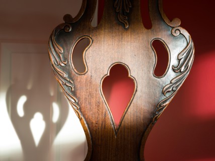 Antique wood chair back with cut out decoration in the shape of a cartoon face. Corresponding face shadow in the background.