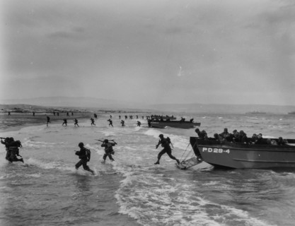Invaders Hit the Shore in Invasion Maneuvers - American troops, carrying rifles and light fighting equipment, spring through the surf from Coast Guard-manned landing craft in final amphibious maneuver...