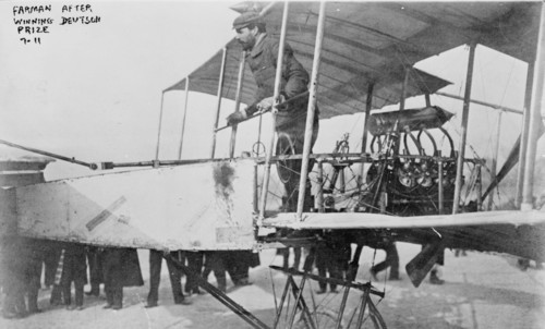 Farman after winning Deutsch prize, Henri Farman, full-length portrait, standing at wheel of airplane, facing left., 1911(?), Farman, Henri, 1873, Photographic prints, 1910-1920., Portrait photographs...