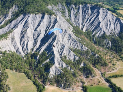 AIR-TO-AIR VIEW. Paraglider soaring above a landscape of eroded ravines. Barcelonnette, Alpes-de-Haute-Provence, France.