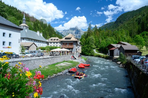 People adventure rafting on stream flowing through town in mountain valley.  Beauty of Giffre mountains region, France.