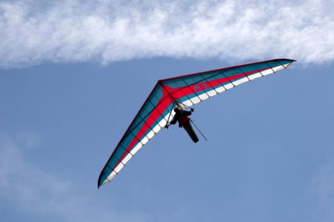 Hang gliding pilot flying blue red and white hang glider against sky in mountains of French Alps Haute Savoie France