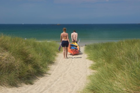 France, Quiberon couple dragging kayak through sand dune towards the sea