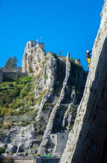 Rock climber in yellow climbing in canyon with castle beyond