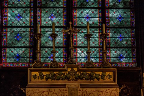 Alter candles in brass candler holders with a  stunning blue and green stained glass window behind in Notre Dame Cathedral ,Paris