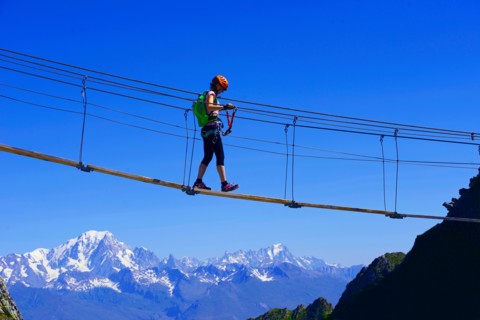 woman crossing a simple suspension bridge, Via Ferrata of La Plagne, Mont Blanc in background, France, Savoie, Tarentaise