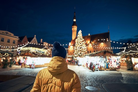 Rear view of man in warm clothing during night walk in city. Traditional Christmas market on Town Hall Square in Tallinn, Estonia.