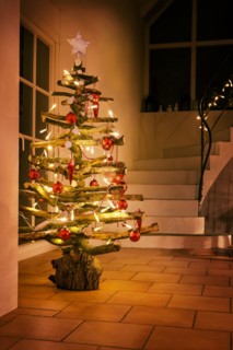 Rustic Christmas tree made of raw wood branches decorated with glowing fairy lights and red balls in a stairwell at night, selected focus, narrow dept