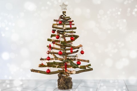 Alternative homemade Christmas tree made of rustic raw wood branches, with fairy lights and red baubles, sustainable craft for eco friendly holidays,